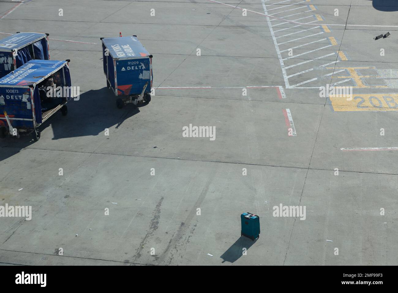 Ein Koffer auf dem Asphalt neben den Gepäckfahrzeugen des Flughafens am Delta Air Lines Terminal im JFK International Airport.New York City.USA Stockfoto