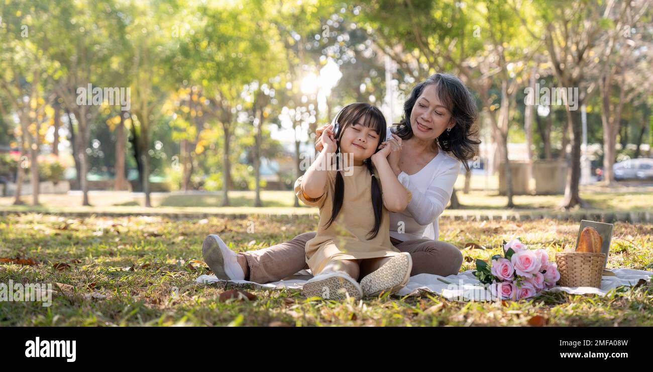 Fröhliche asiatische Großmutter, die mit ihrer reizenden Enkelin zusammen im Park picknickt. Freizeit- und Familienkonzept Stockfoto