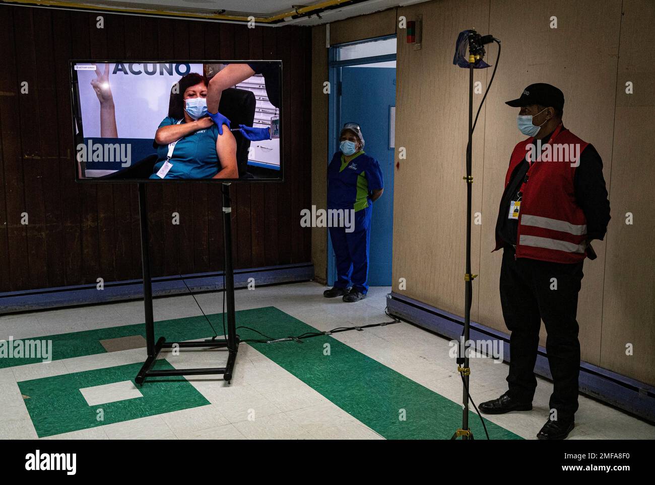 A security guard watches a monitor that shows a live feed of healthcare workers receiving a second dose of the COVID-19 vaccine at the Metropolitan Hospital in Santiago, Chile, Thursday, Jan. 14, 2021. (AP Photo/Esteban Felix) Stockfoto