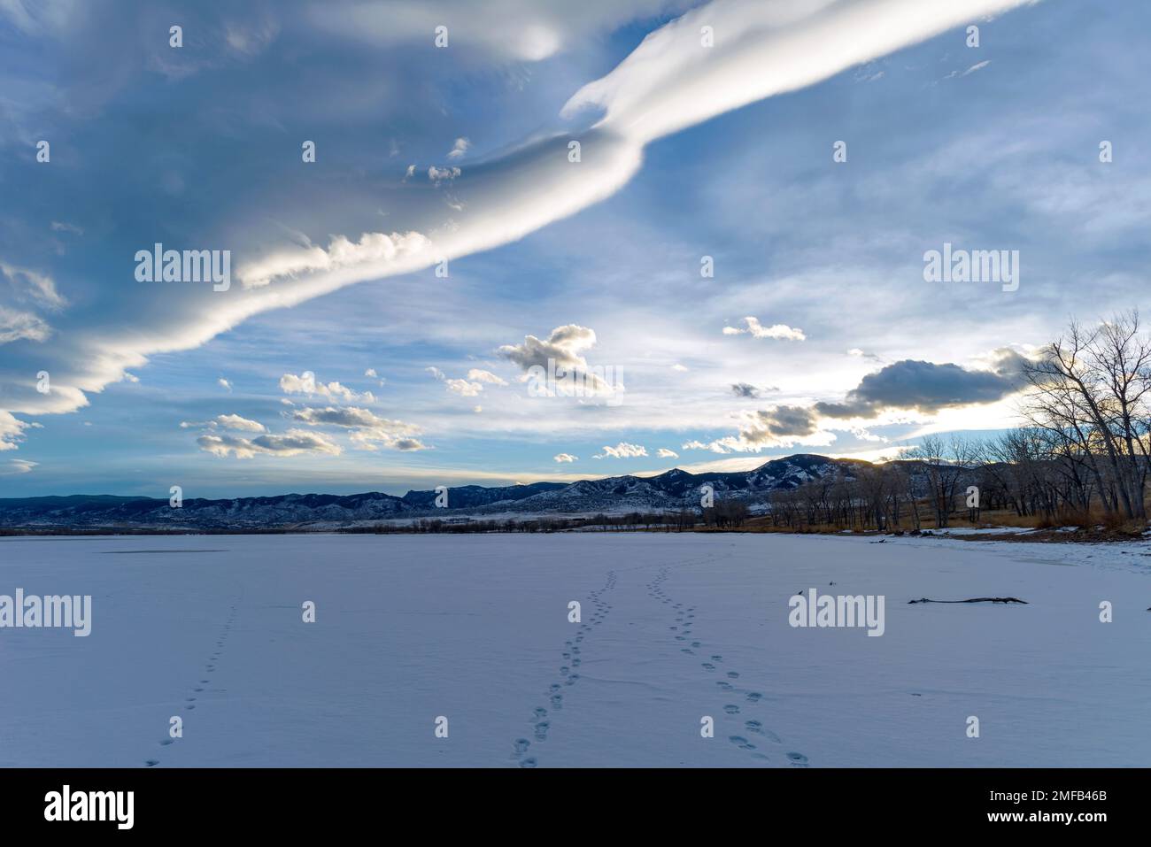 Winter Lake: An einem kalten und windigen Winterabend wurden drei Fußabdrücke auf einem gefrorenen, schneebedeckten Bergsee hinterlassen. Chatfield State Park, CO, USA. Stockfoto