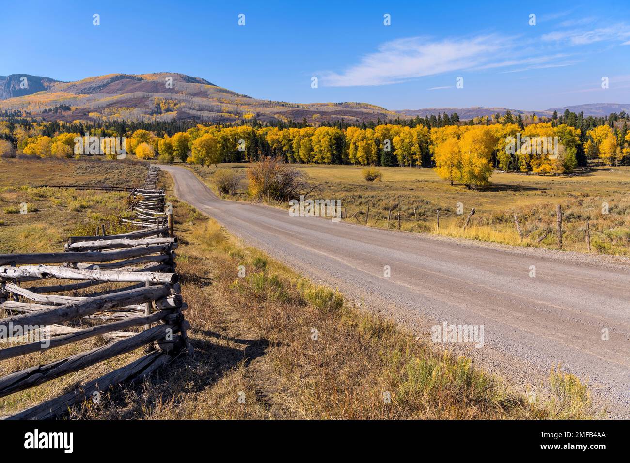 Herbstlandstraße - Weitwinkelblick auf eine Landstraße, die Teil der Owl Creek Pass Road ist und durch hügeliges Ranchland und farbenfrohe Wälder verläuft. Stockfoto