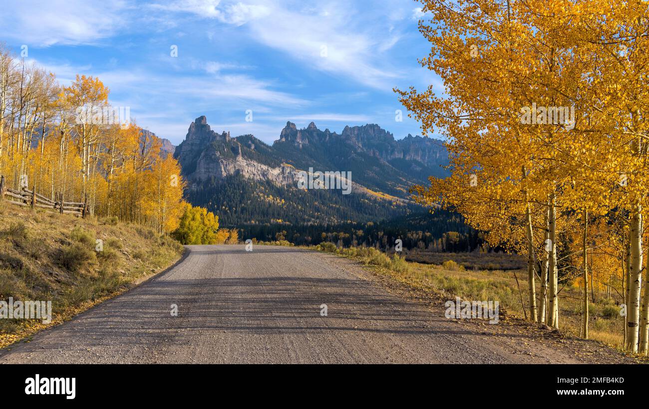 Herbstberg Road - ein abendlicher Herbstblick auf eine Landstraße, die sich in Richtung zerklüfteter Bergkämme erstreckt. Owl Creek Pass Road, Colorado, USA. Stockfoto