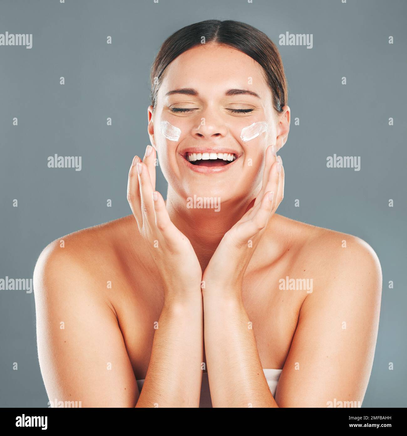 Frau trägt Creme für Gesicht, fröhliches Lachen und Schönheit, Hautpflege und Feuchtigkeitscreme auf, isoliert im Studiohintergrund. Sonnencreme, Lotion und gesunde Haut mit Stockfoto