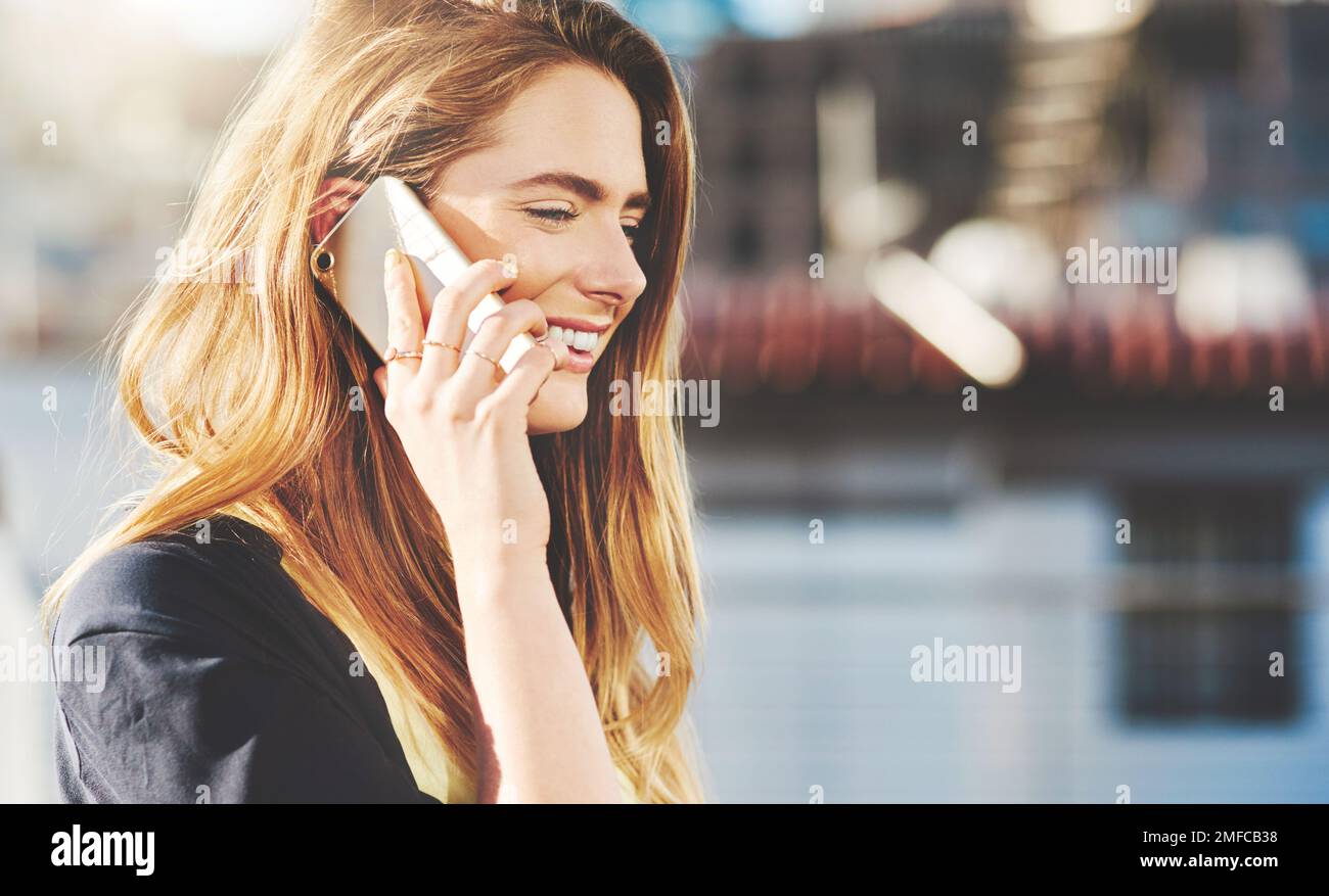 Schön, von Ihnen zu hören. Eine attraktive junge Frau, die telefoniert, während sie draußen steht. Stockfoto