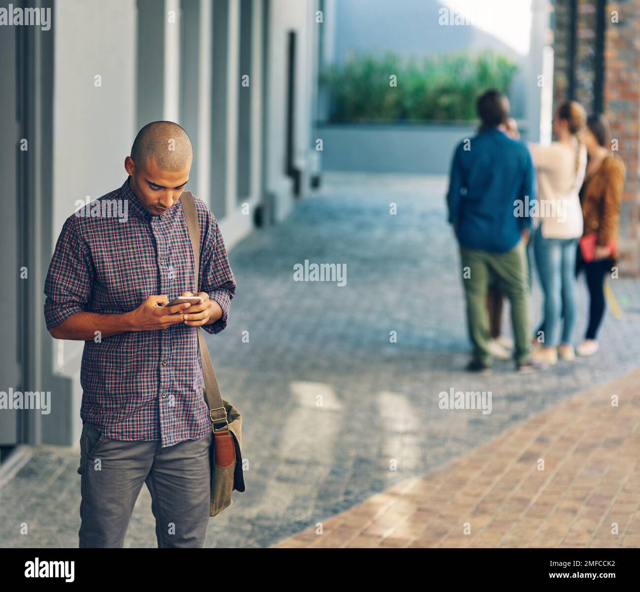 Status-Update das neue Semester hat offiziell begonnen. Ein junger Mann, der draußen auf dem Campus ein Handy benutzt. Stockfoto
