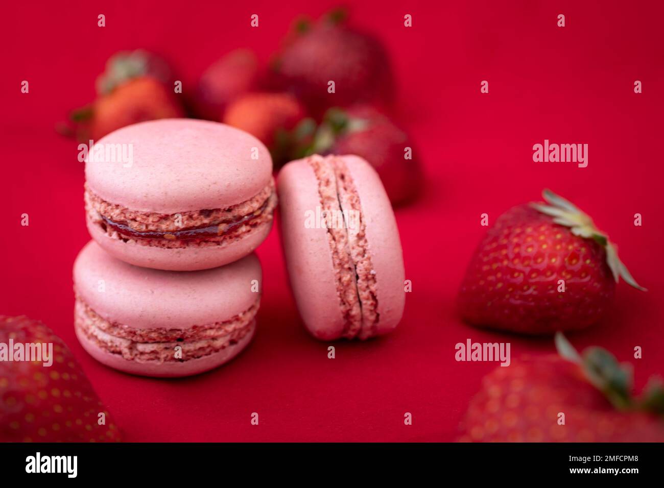 Ein Landschaftsbild eines Studios mit leckeren, bunten französischen Makronen-Keksen auf rotem Hintergrund mit Erdbeeren. Stockfoto