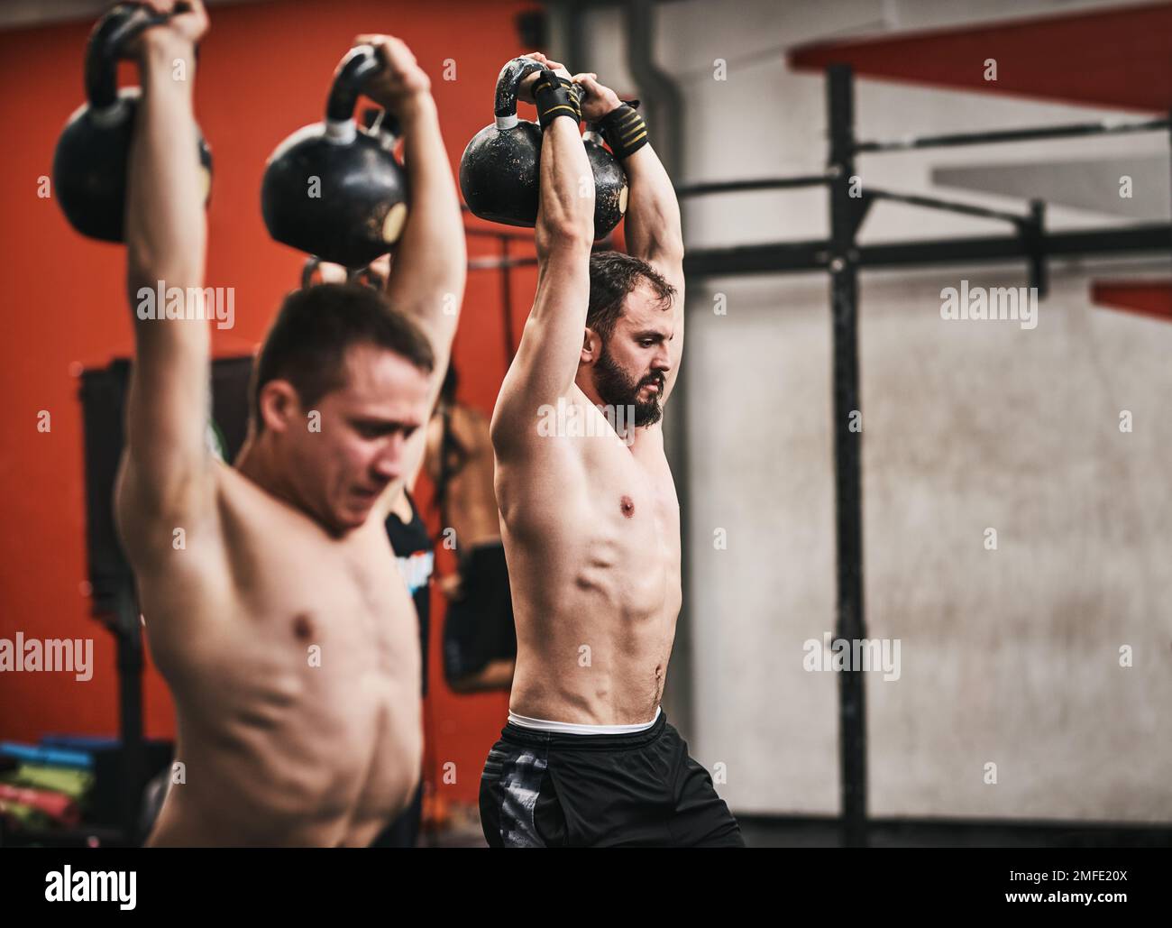 Wir arbeiten zusammen für den Körper, den wir wollen. Junge Männer, die in einem Fitnessstudio Kugelhanteln heben. Stockfoto