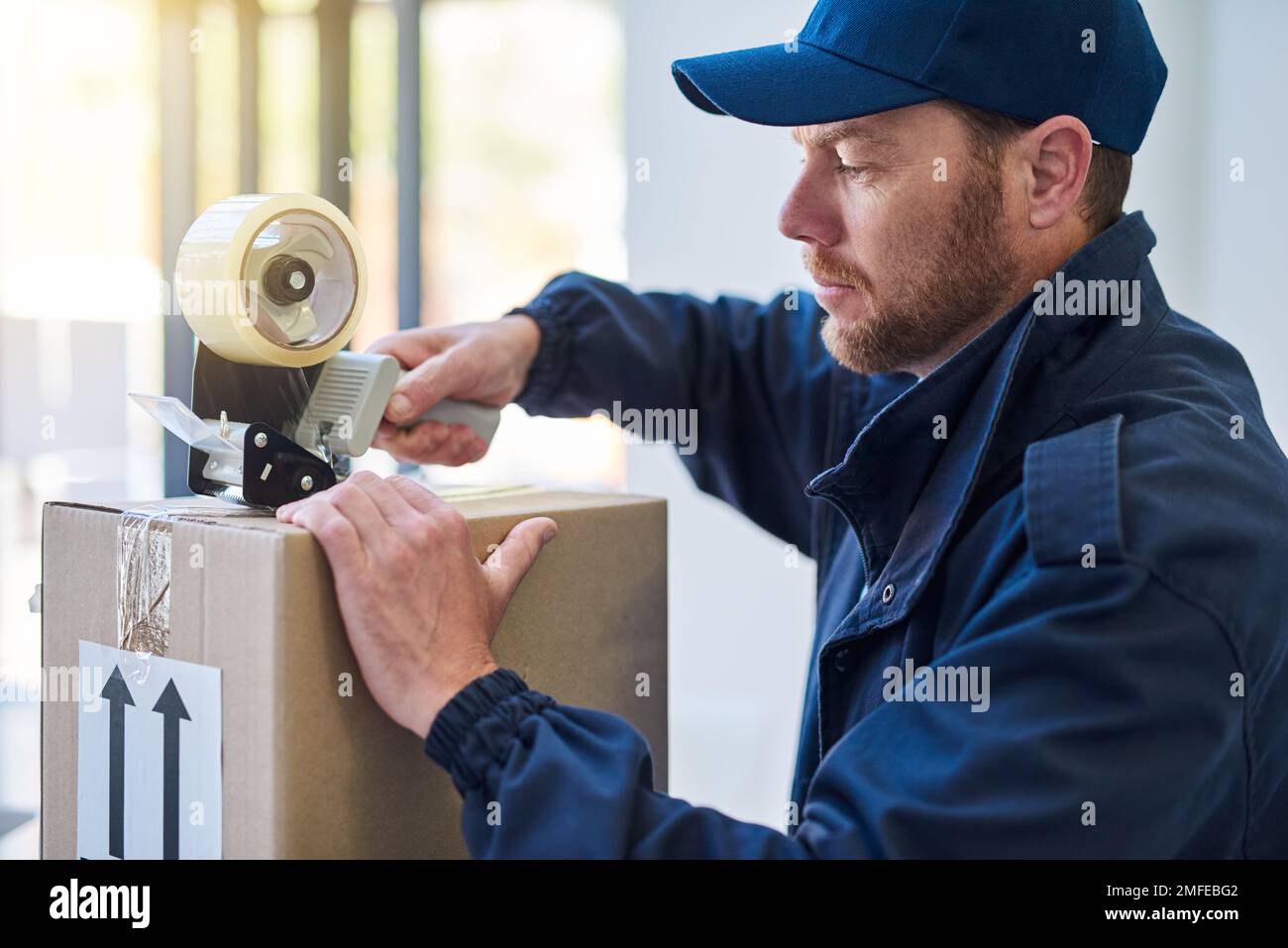 Sicherstellen, dass sie ordnungsgemäß abgedichtet sind. Ein gutaussehender Liefermann, der ein Paket versiegelt, während er ausliefert. Stockfoto
