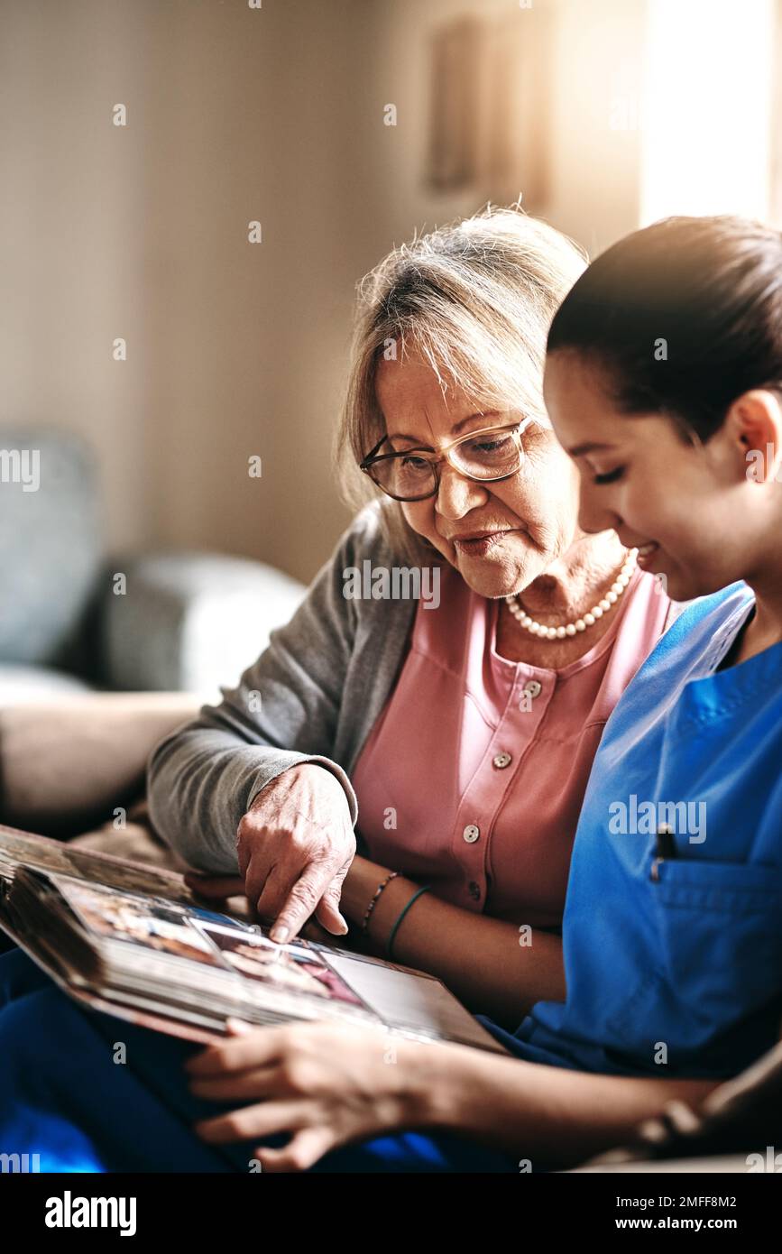 Alte Erinnerungen besuchen. Eine Krankenschwester und eine Seniorin, die zusammen ein Fotoalbum anschauen. Stockfoto