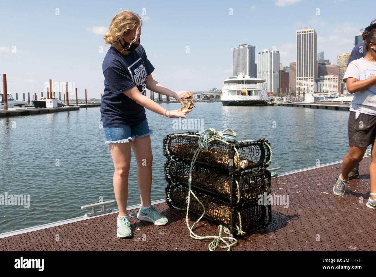 Billion Oyster Project workers place oysters in the water from a pier
