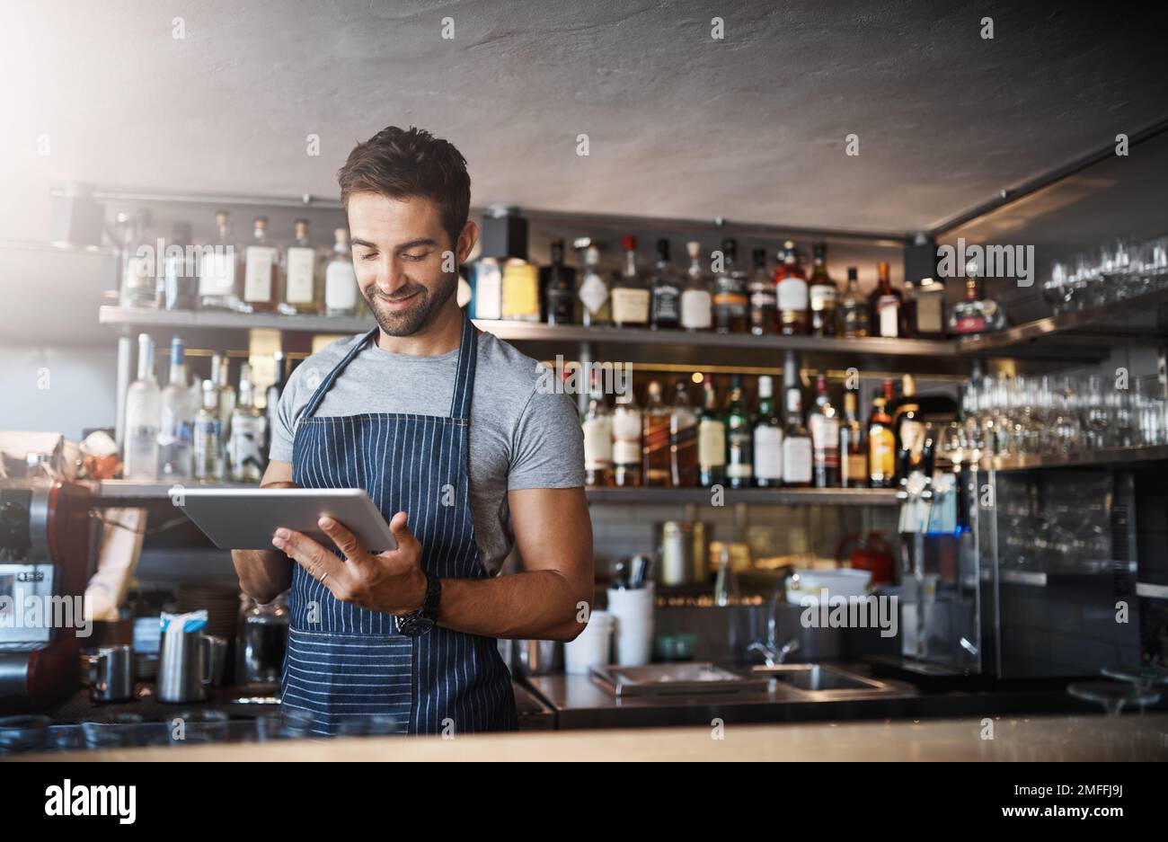 Der digitale Barkeeper. Ein junger Mann, der ein digitales Tablet benutzt, während er hinter einer Theke arbeitet. Stockfoto