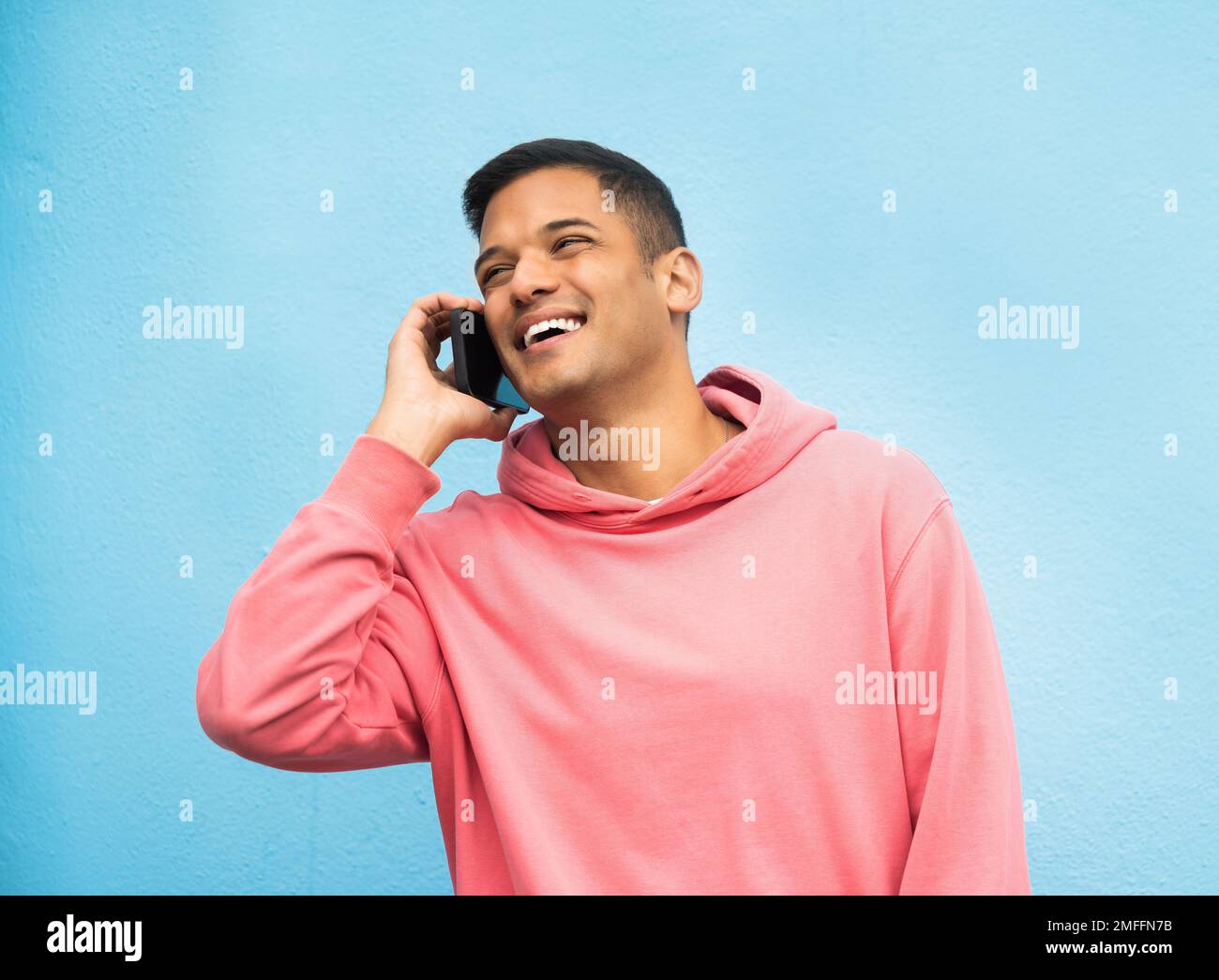 Gelegenheitsmann, Anruf und Lachen in Kommunikation, isoliert auf blauem Hintergrund. Glücklicher Mann, Person oder Jungs mit rosa Jacke in der Diskussion Stockfoto