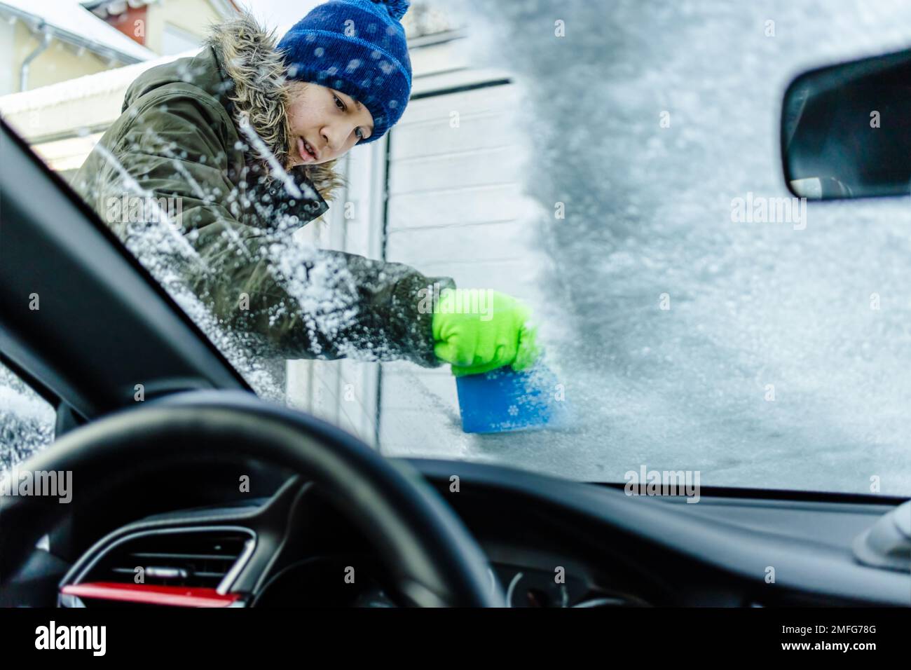 Teenager reinigt das Auto nach einem Schneefall, entfernt Schnee und kratzt Eis Stockfoto