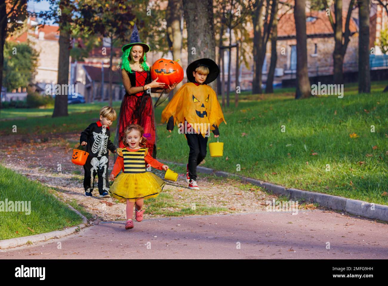 Mutter geht mit Kindern in Halloween-Kostümen und hält Süßigkeiten-Eimer Stockfoto