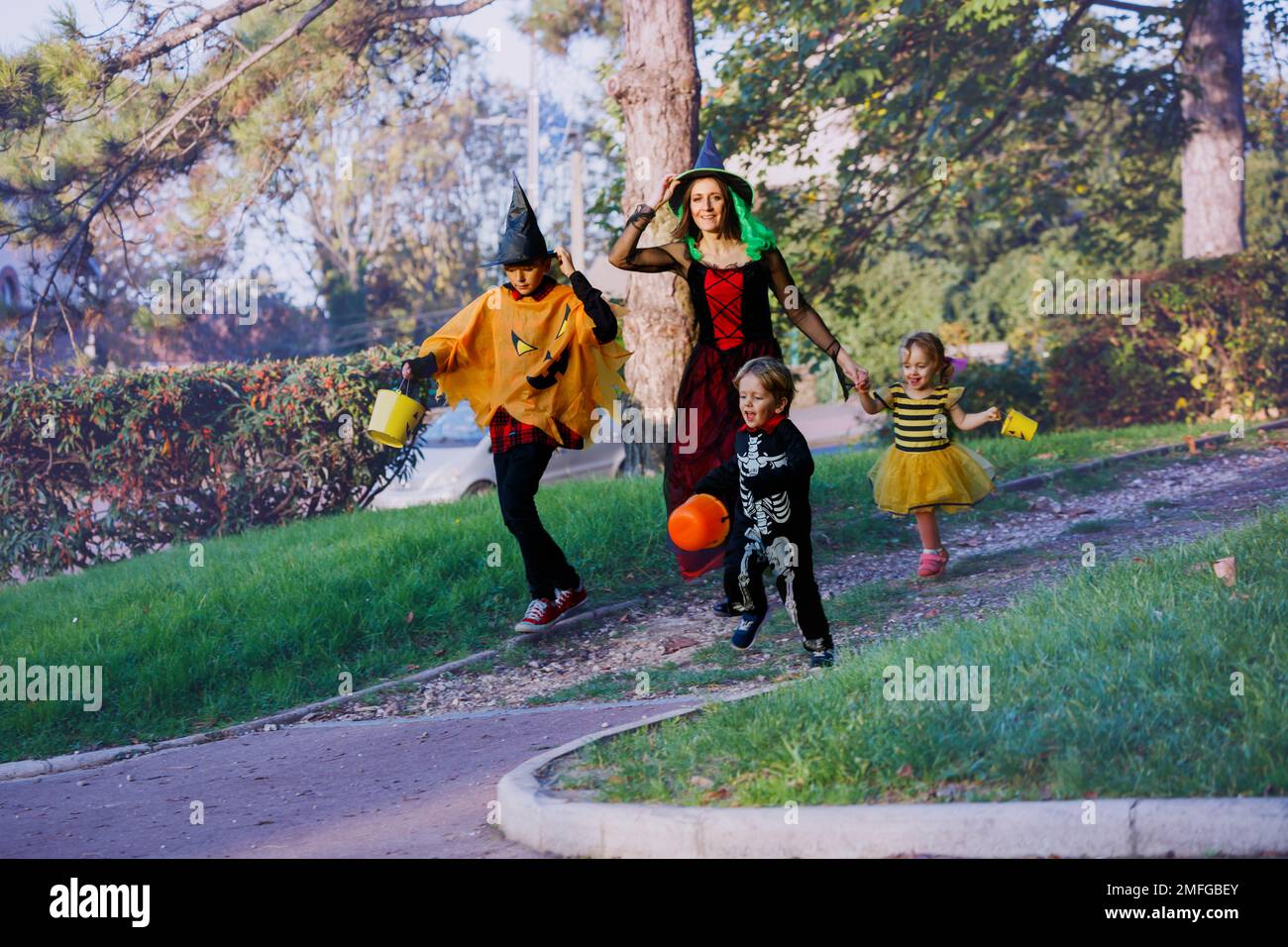 Die Familie läuft zusammen in Halloween-Verkleidungen und hält Süßigkeiten-Eimer Stockfoto