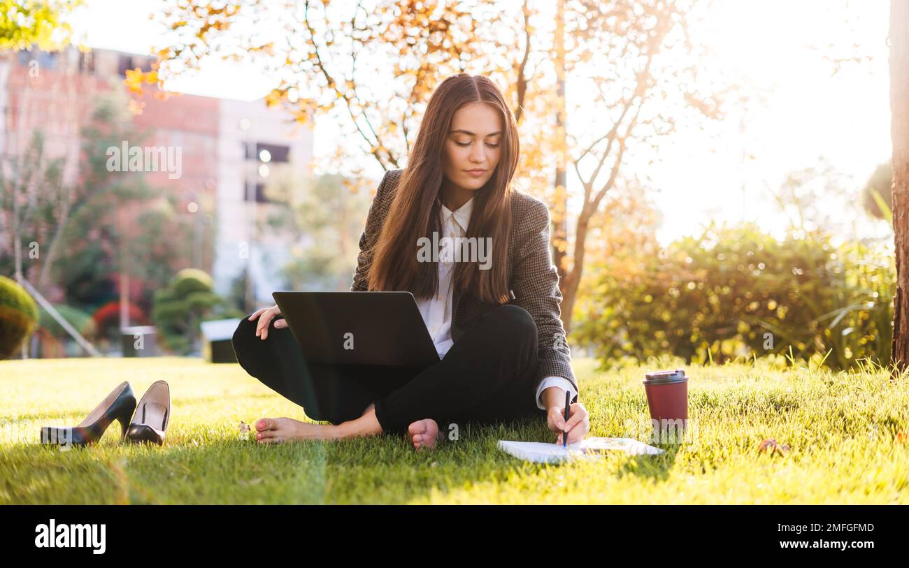 Ganzkörperfoto einer jungen Frau mit Laptop, die auf einer grünen Wiese im Park sitzt. Online-Kommunikation. Geschäftsleute. Geschäftlich Stockfoto