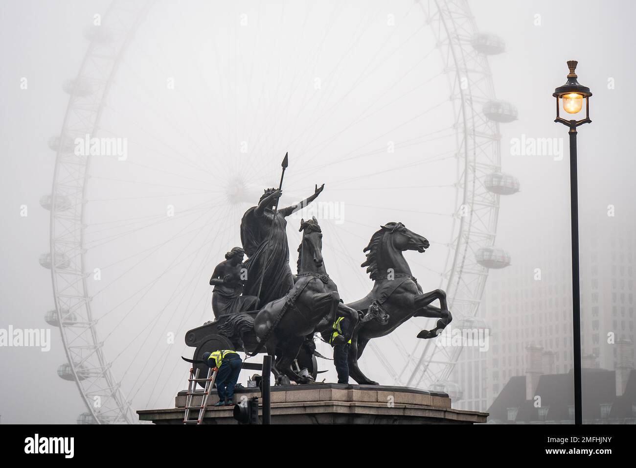 Arbeiter reinigen die Statue des Boudiccan Rebellion am Victoria Embankment, während Nebel das London Eye von lastminute.com am Südufer der Themse in London umgibt. Bilddatum: Mittwoch, 25. Januar 2023. Stockfoto
