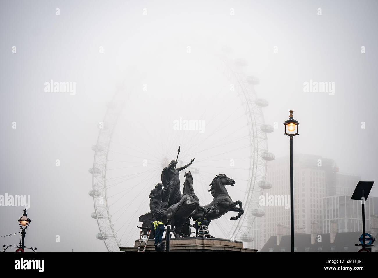 Arbeiter reinigen die Statue des Boudiccan Rebellion am Victoria Embankment, während Nebel das London Eye von lastminute.com am Südufer der Themse in London umgibt. Bilddatum: Mittwoch, 25. Januar 2023. Stockfoto
