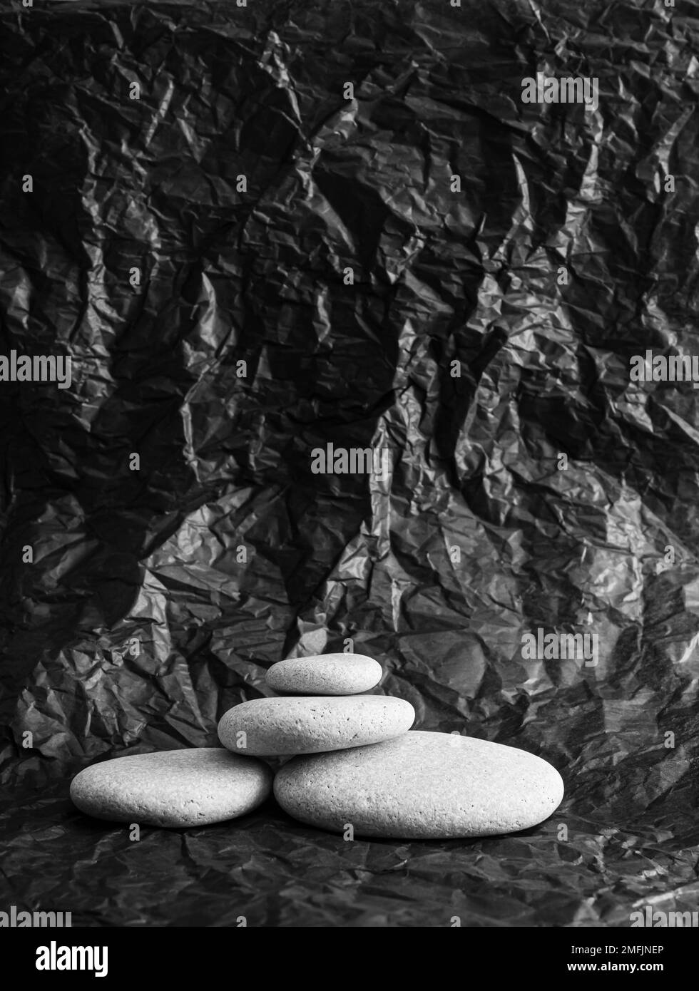 Graue, flache Steine auf schwarz gestapelt zerknitterte abstrakte Seidenpapierprodukte Werbetintergrund, seitliches Studiolicht. Viel Platz zum Kopieren. Stockfoto