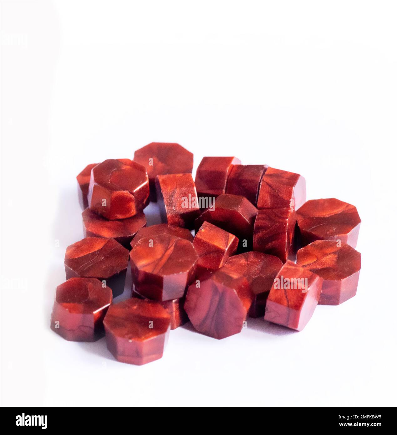Rotes Wachs schmilzt auf weißem Hintergrund und wird für verschiedene Zwecke wie Dekoration, Versiegelung von Flaschen, Kunst- und Handwerksprojekte, Einladungen und Hochzeitsfavoriten verwendet Stockfoto
