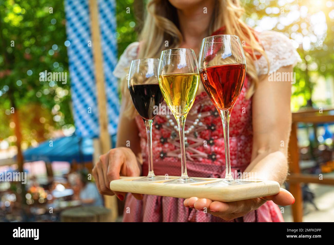 Die Kellnerin bringt verschiedene Weinsorten in Gläsern durch einen bayerischen Biergarten oder ein oktoberfest Stockfoto