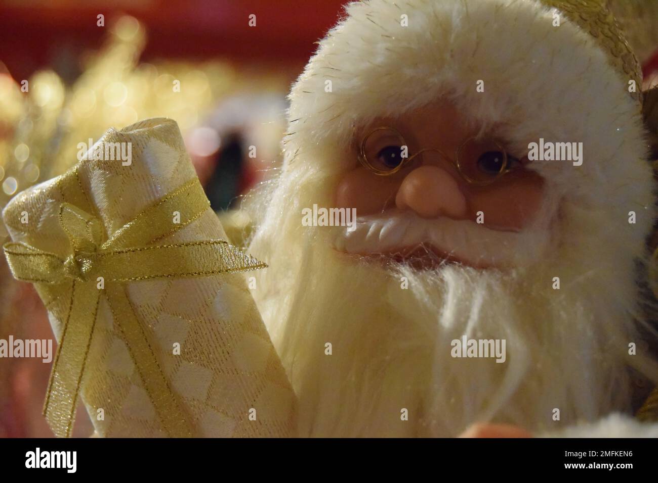 Ein traditionelles Weihnachtsmann-Weihnachtsdekorat in Creme und Gold mit weißem Bart und goldenen Gläsern und einem eingewickelten Weihnachtsgeschenk. Stockfoto