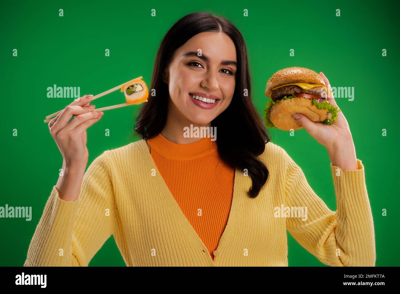 Eine fröhliche Frau hielt leckere Burger und frisches Sushi, während sie auf ein grünes Bild in die Kamera schaute Stockfoto