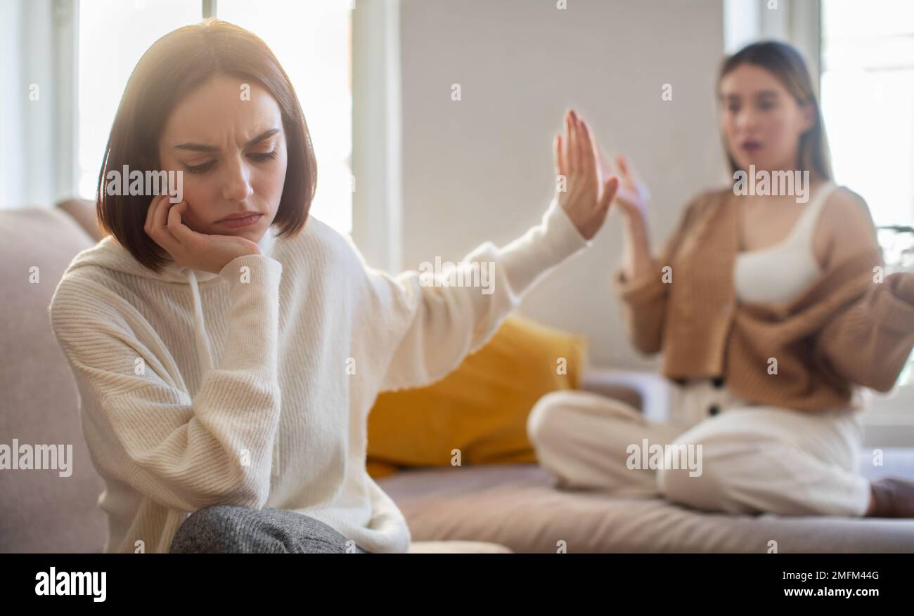 Beleidigte traurige europäische Millennials-Dame ignoriert schreiende unzufriedene Freundin, die mit der Hand ein Stoppschild macht Stockfoto