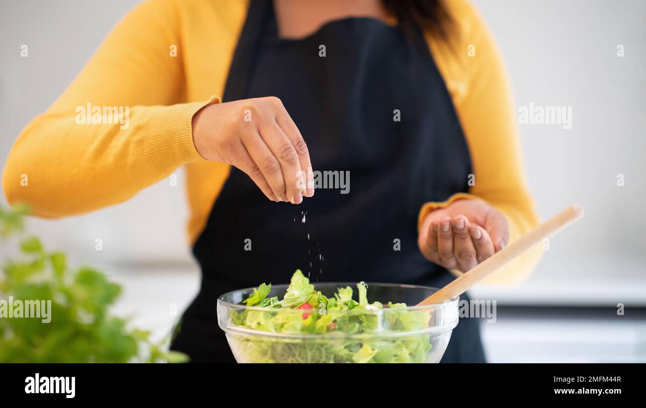 Eine afroamerikanerin der Jahrtausendwende mit Salat aus Schürze, kocht Abendessen am Tisch mit frischem Bio-Gemüse Stockfoto