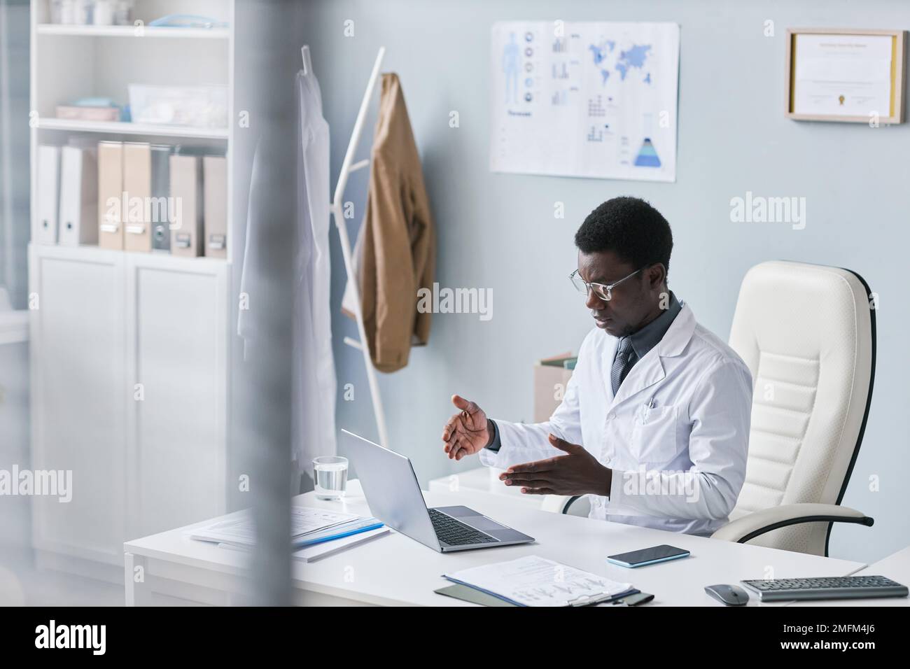 Hochwinkelporträt eines jungen schwarzen Arztes in der Online-Sprechstunde beim Gespräch mit dem Patienten über das Internet am Büroschreibtisch Stockfoto