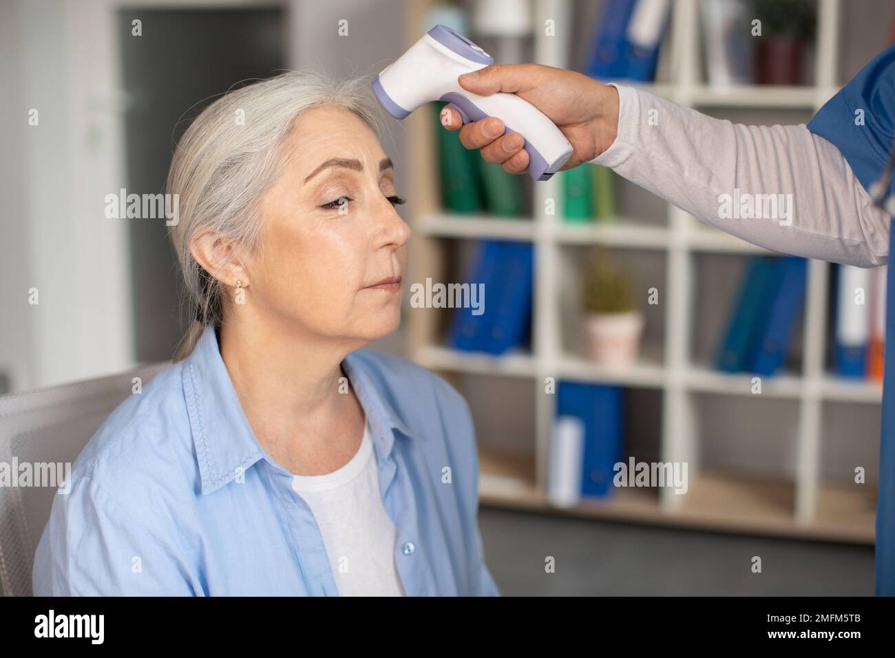 Der Arzt misst die Temperatur mit einem berührungslosen Thermometer bei einer alten Kaukasierin in der Klinik Stockfoto