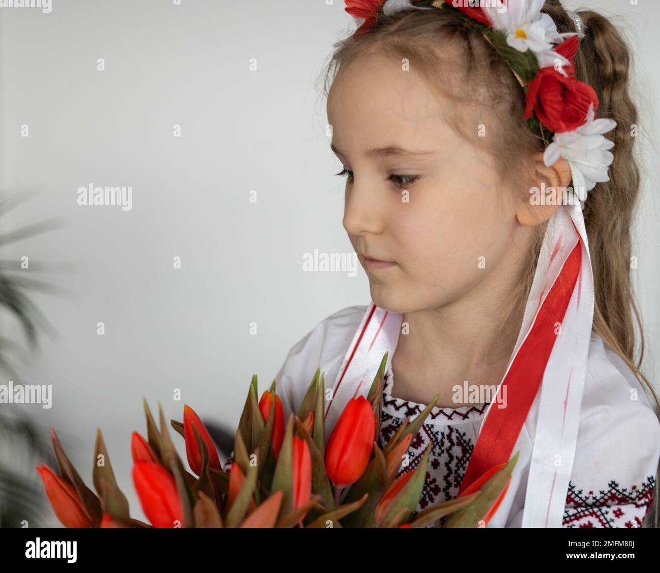 Ein grüblerisches Mädchen in einem ukrainischen Nationaltrikot und einem Strauß roter Tulpen - das Konzept einer friedlichen Ukraine Stockfoto