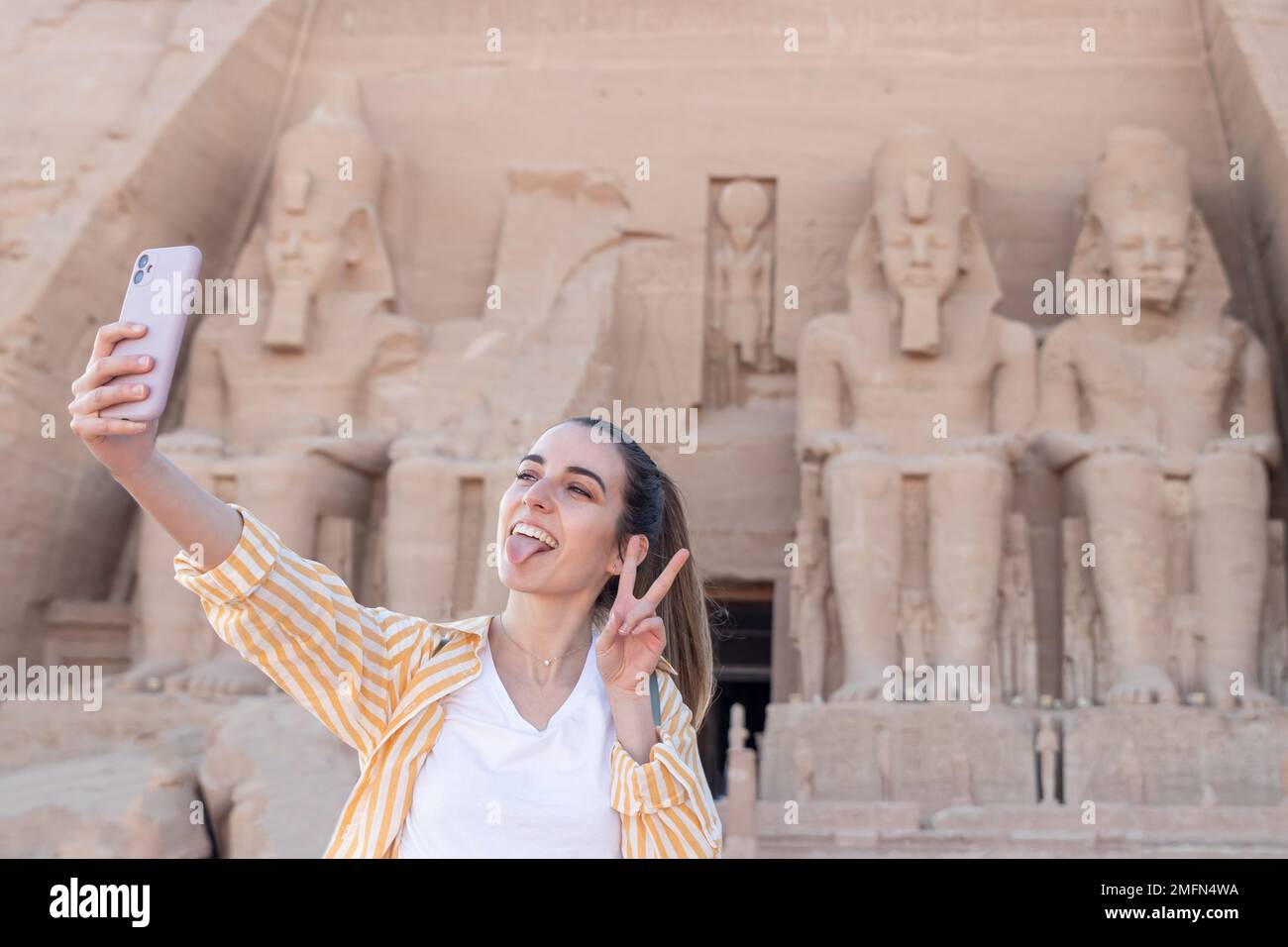 Junge Touristin, die ein Selfie mit Tounge out and peace out Schild in Abu Simbel, Ägypten macht Stockfoto