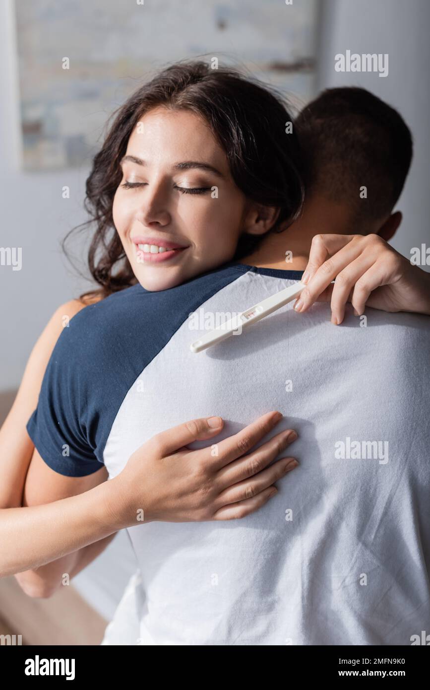 Positive Frau mit Schwangerschaftstest und umarmter Freund zu Hause, Stock Image Stockfoto