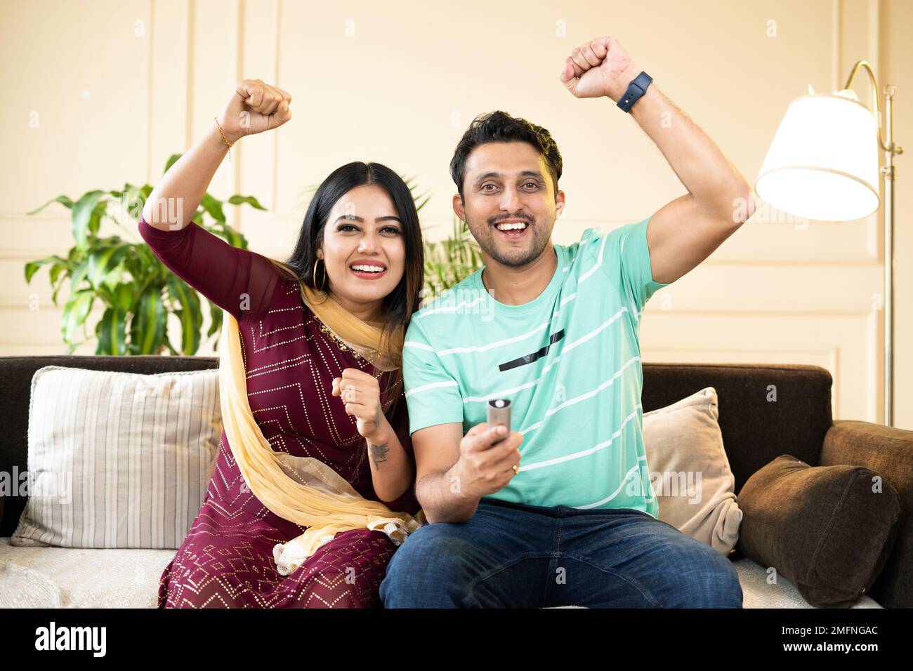 Aufgeregtes, fröhliches Paar, das mit erhobenen Händen schreit, während es zu Hause ein Live-Cricket-Sportspiel im fernsehen oder Fernsehen ansieht - Konzept der Unterhaltung Stockfoto