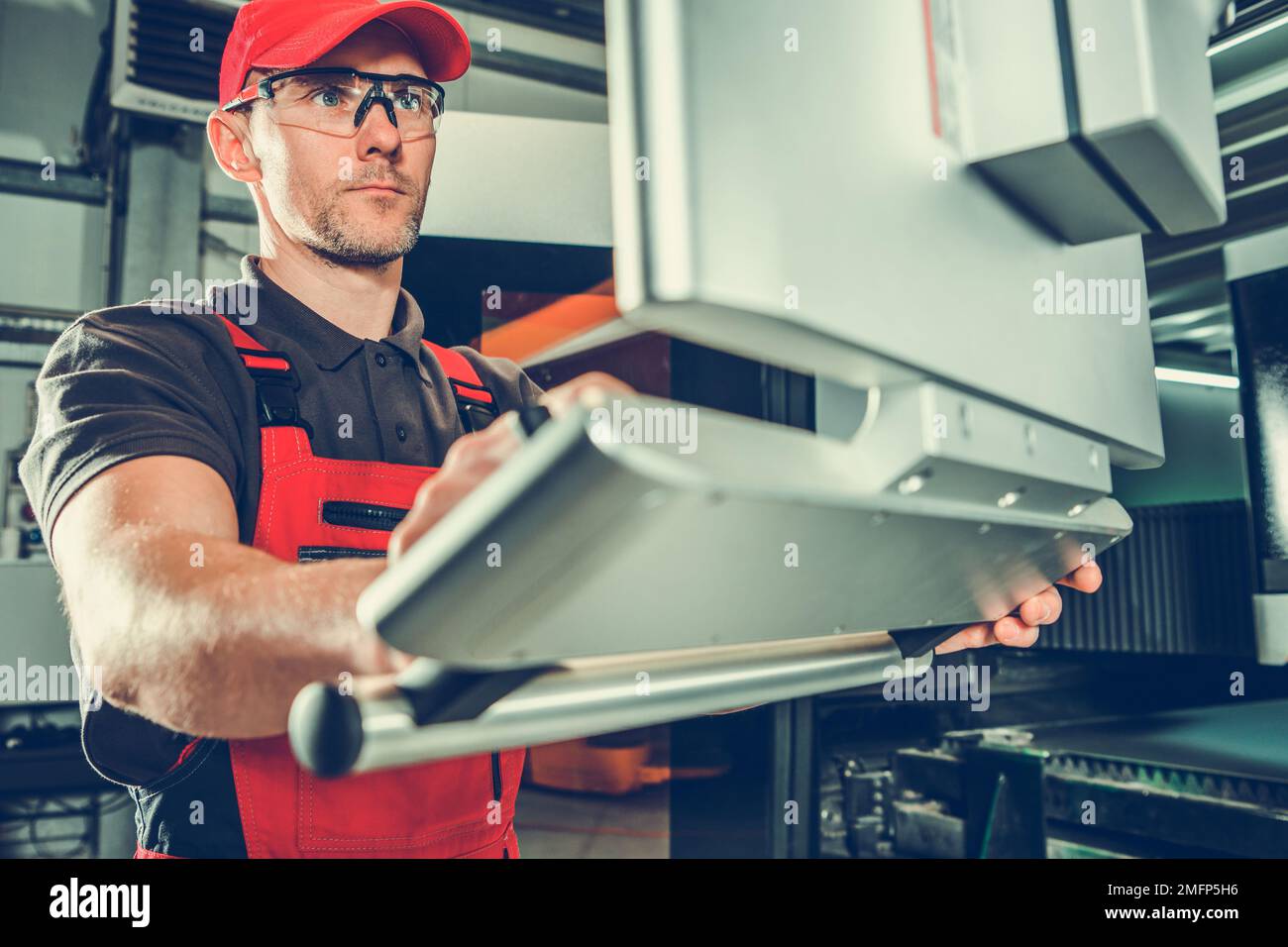 Weißer Metallbearbeiter in seinem 40s, der den Metallschneider mithilfe des integrierten Touchscreens vorbereitet. Metallverarbeitende Industrie. Stockfoto