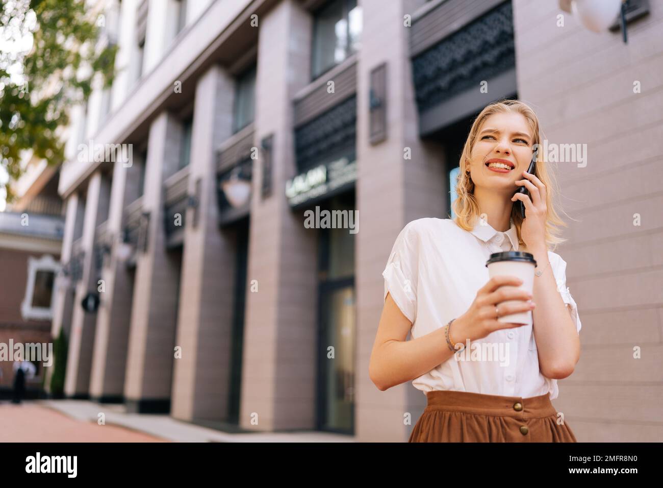 Porträt einer jungen, fröhlichen Frau in legerer Kleidung, die am Sommertag auf der Straße der Stadt auf dem Handy spricht. S Stockfoto