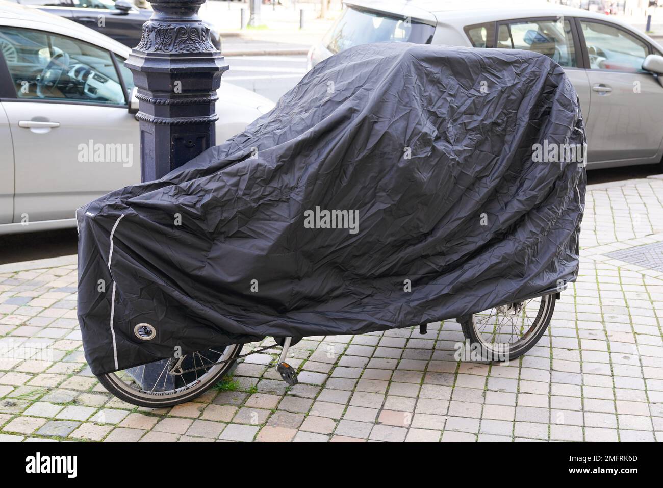 Fahrrad geschützt durch dunkelgraue blaue Schutzhülle Planenjacke Dreiradfahrrad auf der Straße Stockfoto