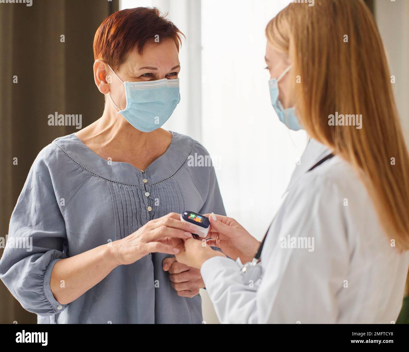 Covid-Aufwachzentrum-Ärztin mit medizinischer Maske, die den Sauerstoffgehalt älterer Patienten prüft Stockfoto
