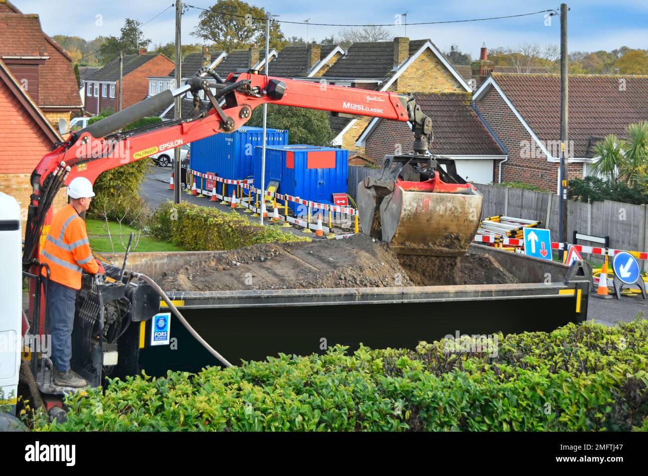 Fahrer von Kipperfahrzeugen stehende Bedienelemente für Kranladerschaufel auf der Rückseite eines Doppellagers neben Straßenarbeiten im Wohngebiet England UK Stockfoto