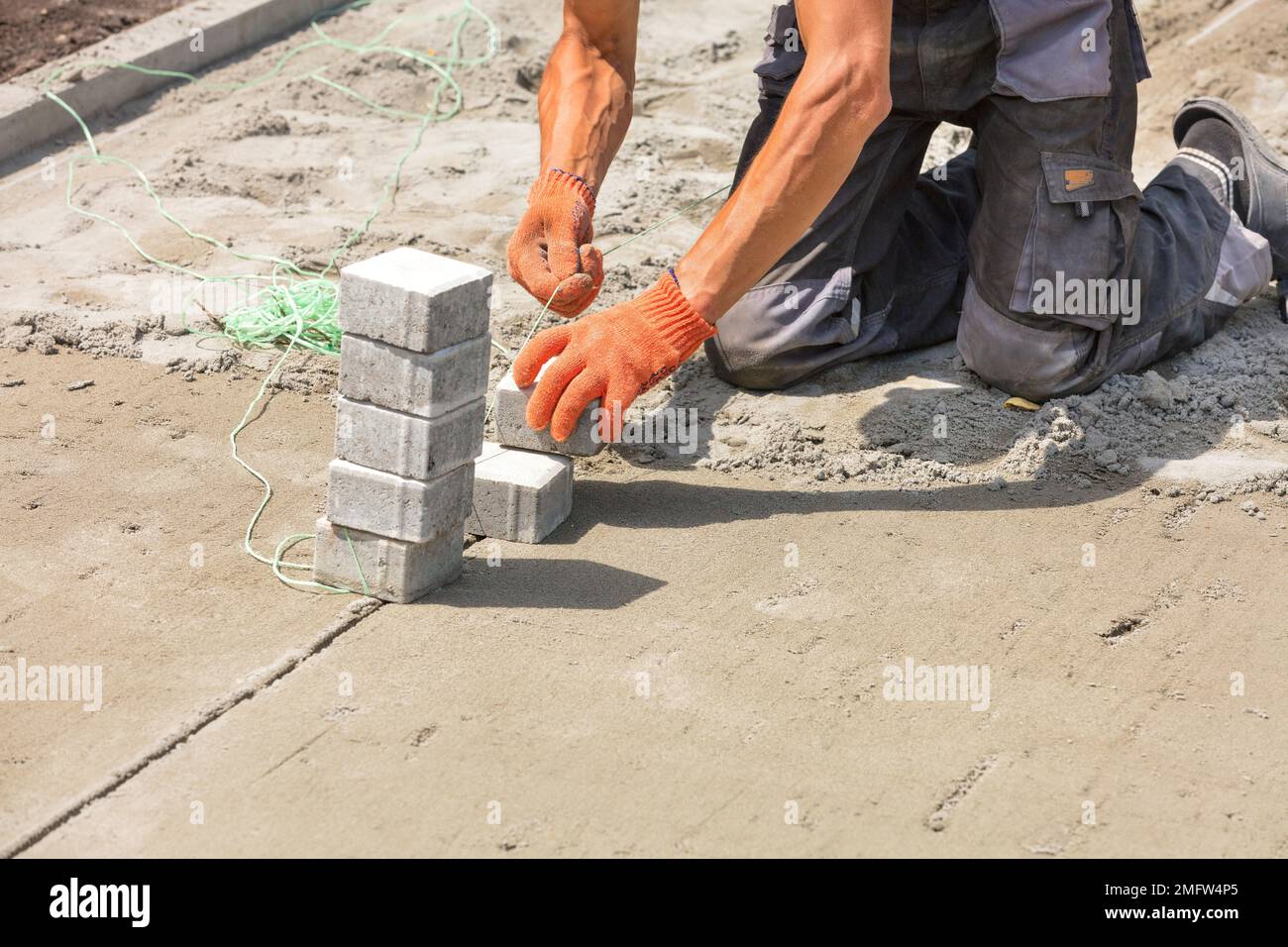 Ein Arbeiter installiert Nylonfäden auf Pflasterplatten auf Sandbasis, um sie später an einem hellen, sonnigen Sommertag zu montieren. Speicherplatz kopieren. Stockfoto