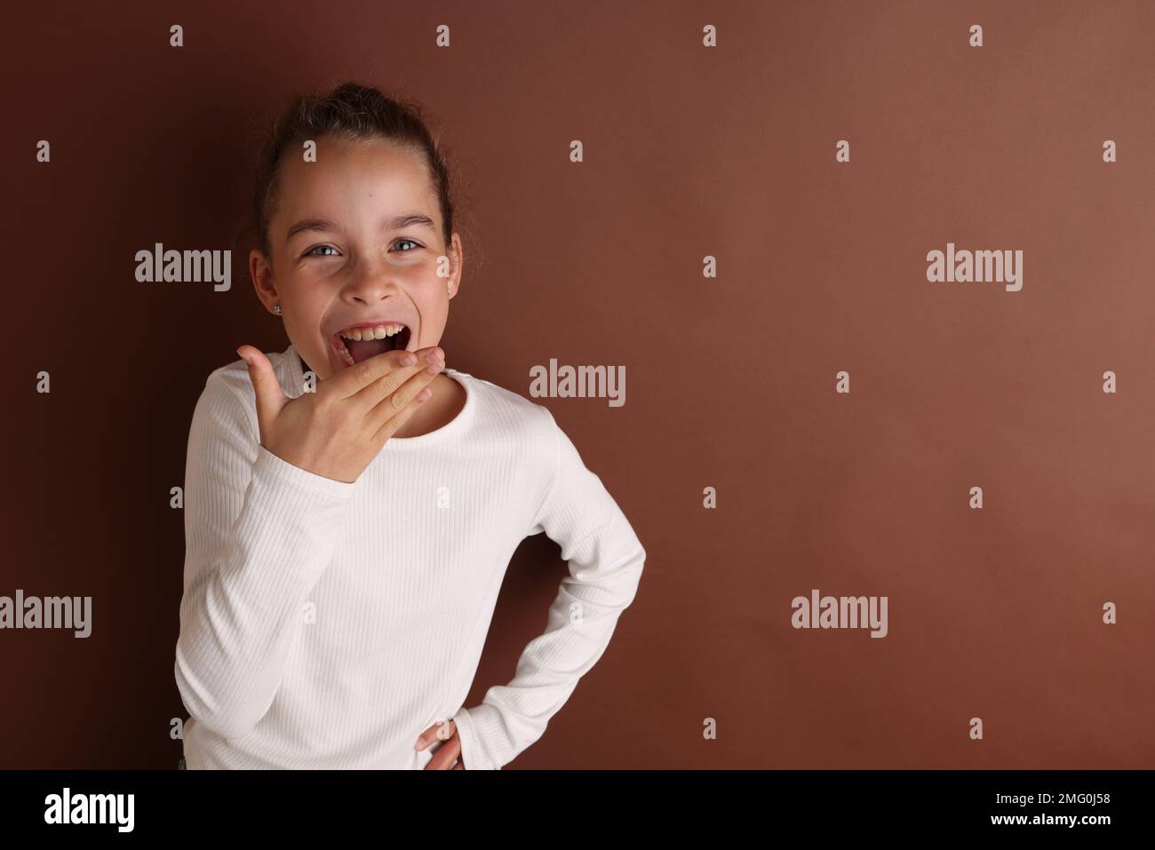 Kleines emotionales Teenager-Mädchen in Weiß, 11 Jahre alt, 12 Jahre alt, auf isoliertem braunen Schokoladen-Hintergrund. Stockfoto