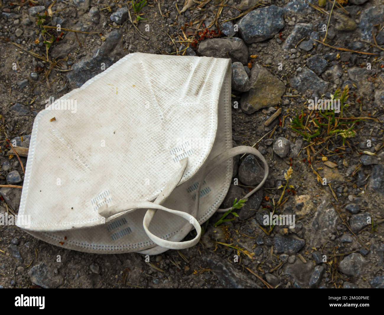 Alte, schmutzige und weggeworfene FFP2-Maske liegt auf der Landstraße. Ein Symbol für Müll und Verschmutzung. Stockfoto