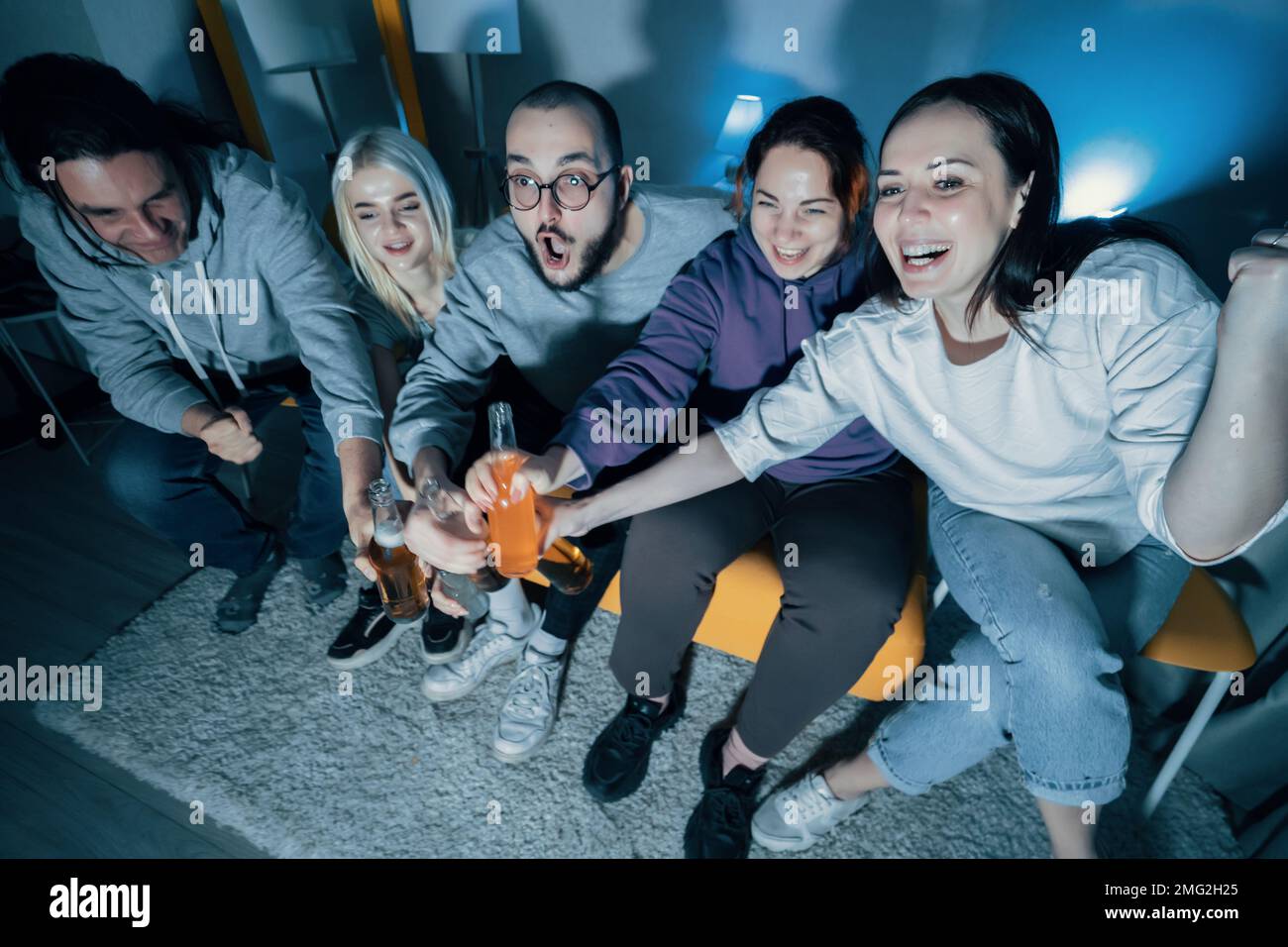 Glückliche Freunde sehen sich zu Hause Fußball oder Fußball im fernsehen an. Feiern mit Flaschen Bier Siegesziel. Stockfoto