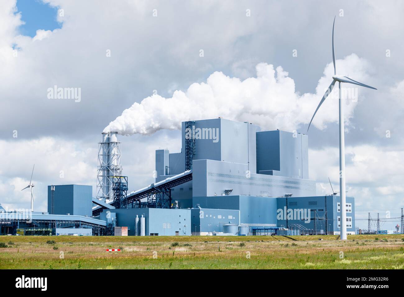 Blick auf ein Kohlekraftwerk mit Biomen, umgeben von Windturbinen an einem bewölkten Sommertag Stockfoto