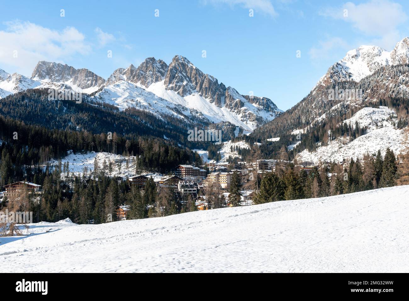 Verschneites Bergdorf, umgeben von majestätischen felsigen Gipfeln an einem sonnigen Wintertag Stockfoto