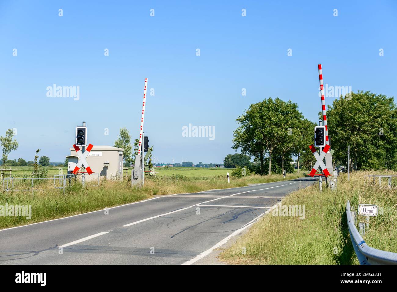 Bahnübergang mit angehobenen Barrieren, damit der Verkehr an einem klaren Sommertag sicher auf dem Land überquert werden kann Stockfoto