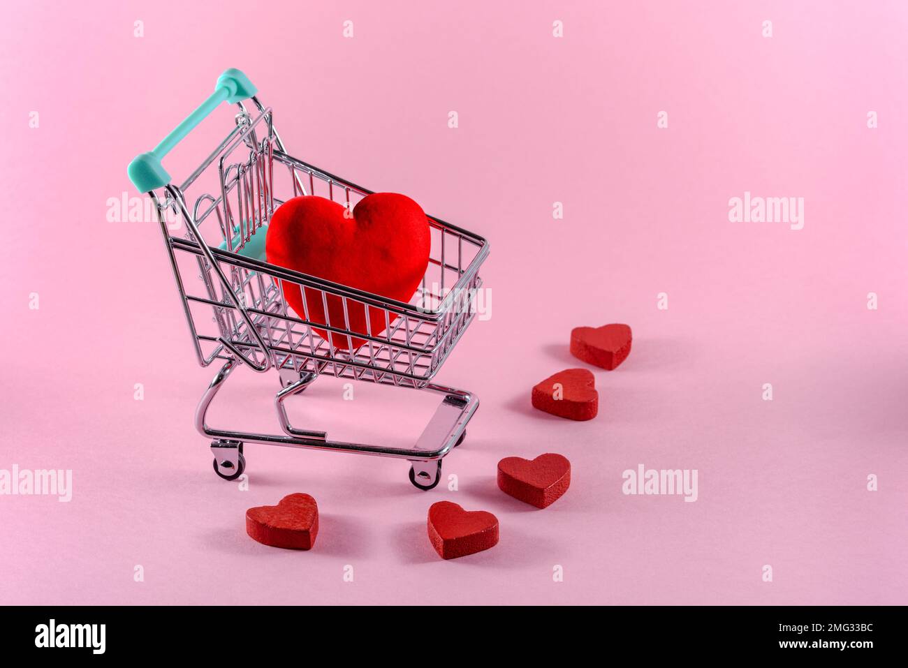 Rotes Herz in einem kleinen Einkaufswagen auf hellrosa Hintergrund. Valentinstag-Shopping-Konzept. Speicherplatz kopieren. Stockfoto