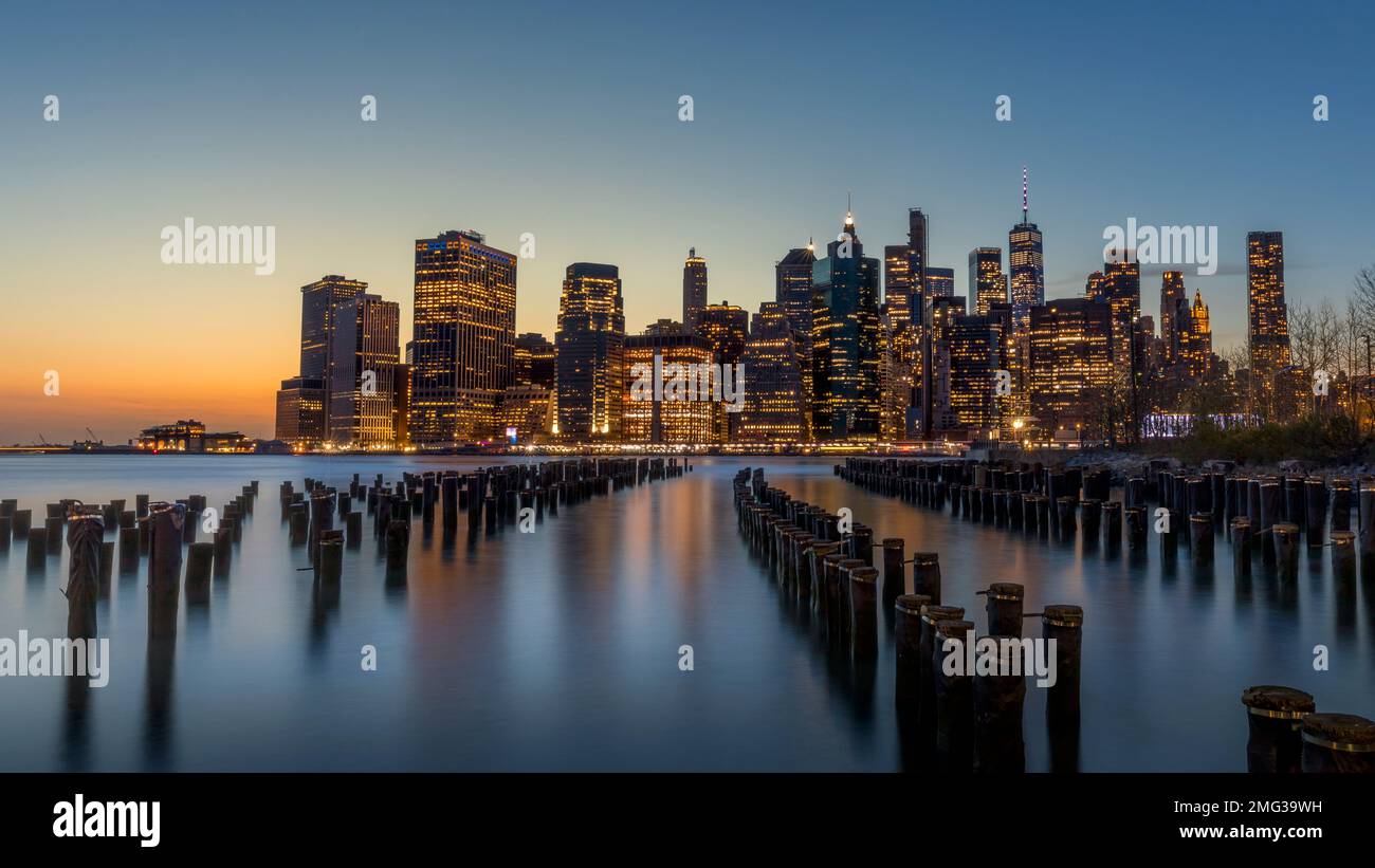 New York, USA - 25. April 2022: Langzeitbelichtung der Skyline von Lower Manhattan bei Sonnenuntergang mit einem alten Brooklyn Pier im Vordergrund Stockfoto