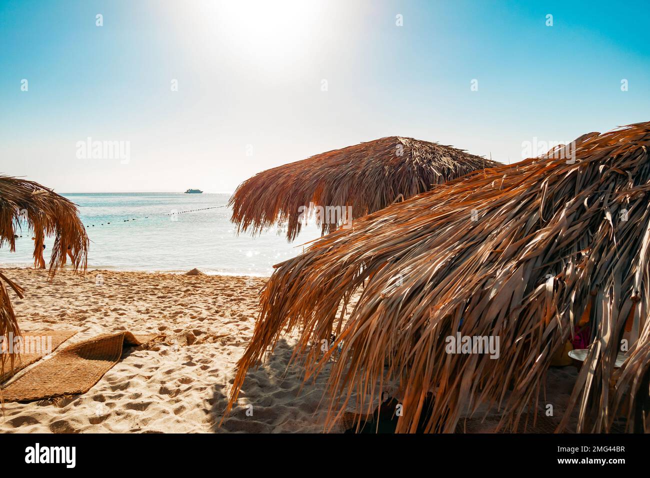 Tropische Strandschirme im Hintergrund des blauen Meeres. Das Dach besteht aus getrockneten Palmenzweigen. Der Begriff Tourismus und Reisen. Stockfoto